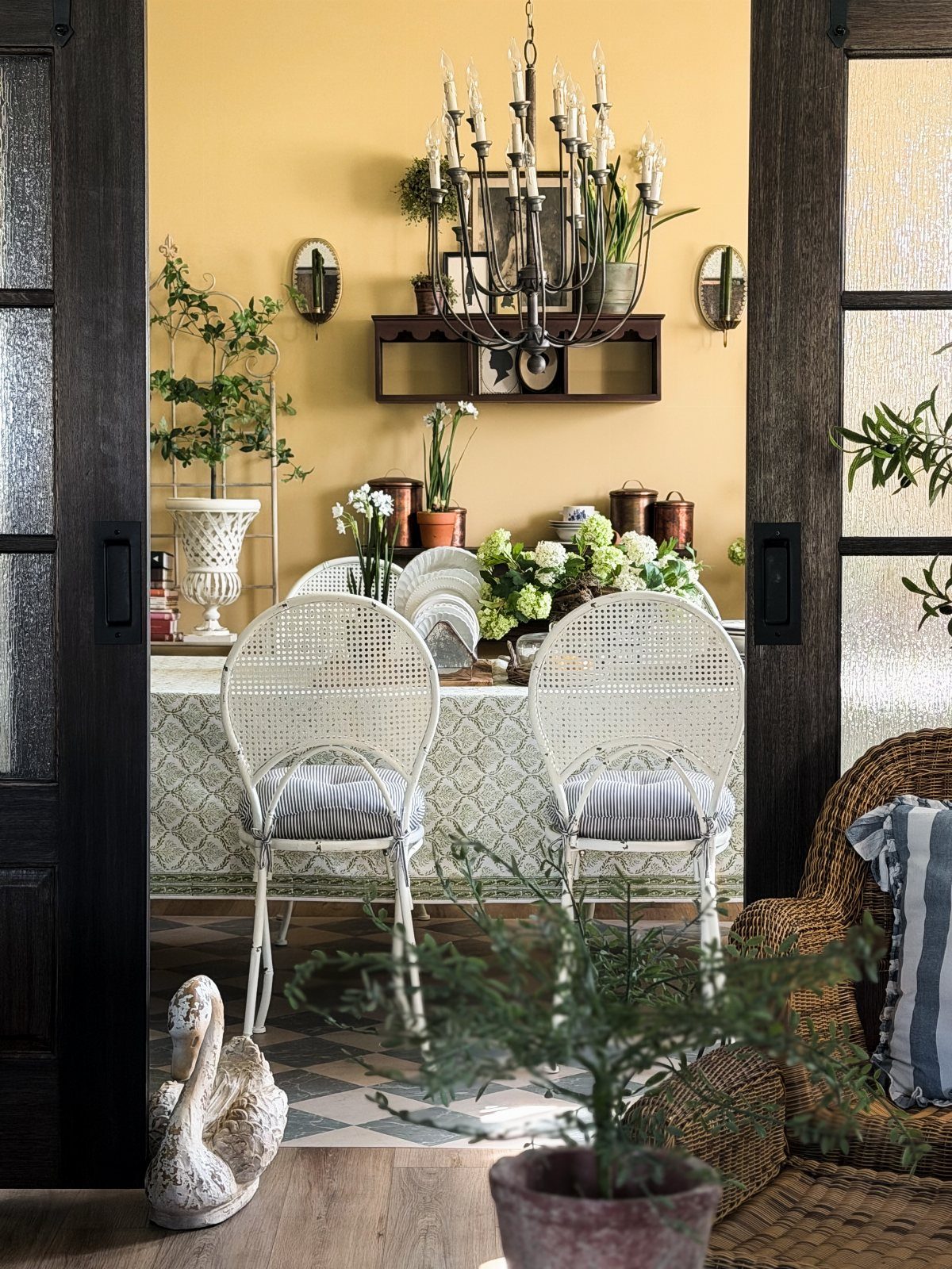 Dining room with warm yellow walls, white wicker chairs, and a candle chandelier.