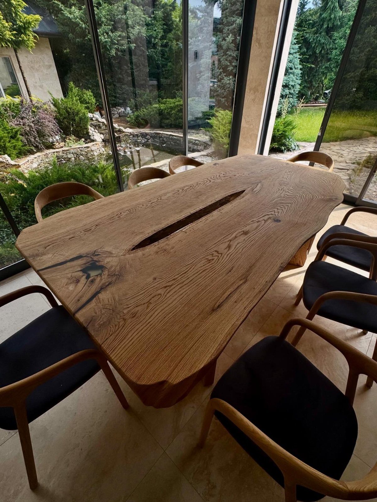 Live edge wood slab dining table with black chairs in a modern sunroom.