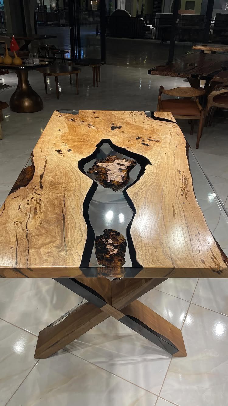 Live edge wood slab dining table with a dark resin river center and X-legs.